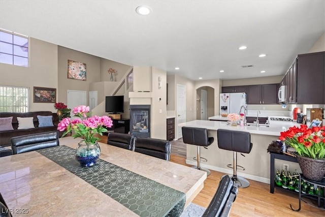 dining area featuring arched walkways, a glass covered fireplace, recessed lighting, and light wood-type flooring