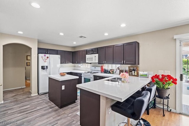 kitchen featuring white appliances, visible vents, a kitchen island, a sink, and light countertops