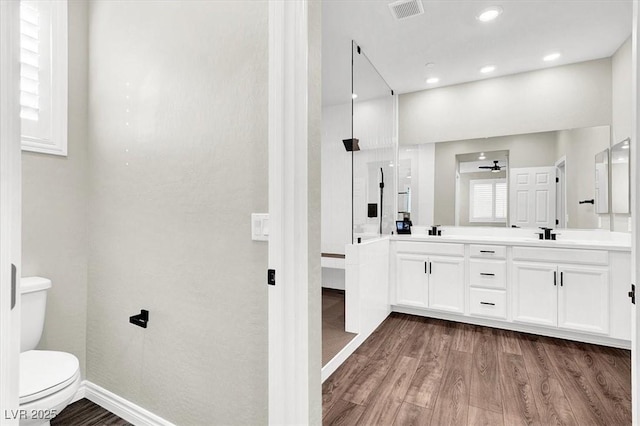 bathroom featuring visible vents, toilet, a sink, wood finished floors, and double vanity