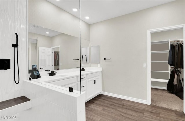 bathroom featuring a walk in closet, baseboards, double vanity, wood finished floors, and a sink