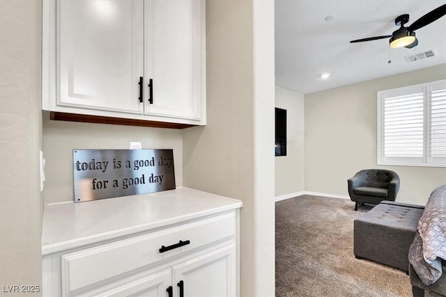 interior space featuring visible vents, open floor plan, carpet flooring, white cabinets, and a ceiling fan