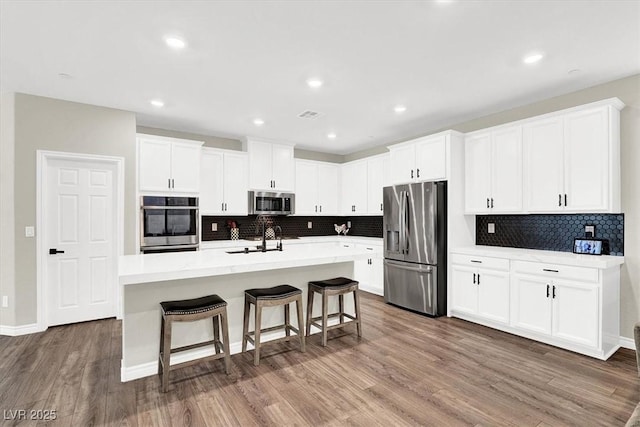 kitchen featuring a center island with sink, a sink, wood finished floors, stainless steel appliances, and a breakfast bar area