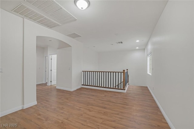 spare room with visible vents, arched walkways, baseboards, and light wood-style flooring