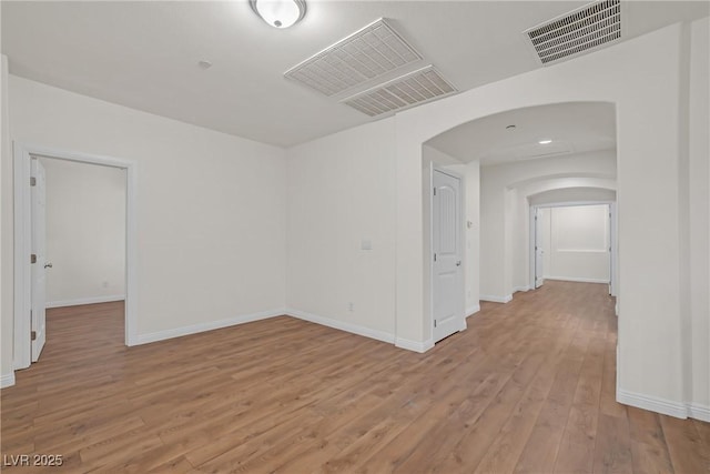 spare room with arched walkways, visible vents, light wood finished floors, and baseboards