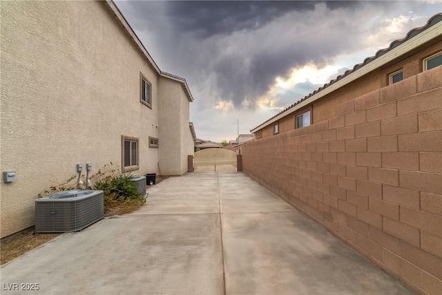 view of side of home with fence, stucco siding, cooling unit, a patio, and a gate