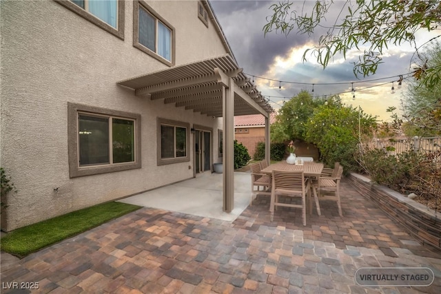 patio terrace at dusk featuring fence, outdoor dining space, and a pergola