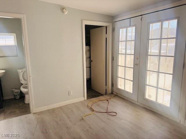 unfurnished bedroom featuring connected bathroom, french doors, baseboards, and wood finished floors