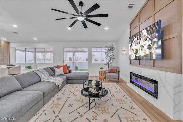 living area featuring a glass covered fireplace, recessed lighting, light wood-style floors, and visible vents