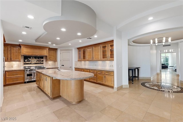 kitchen featuring visible vents, brown cabinets, light stone counters, a sink, and stainless steel stove