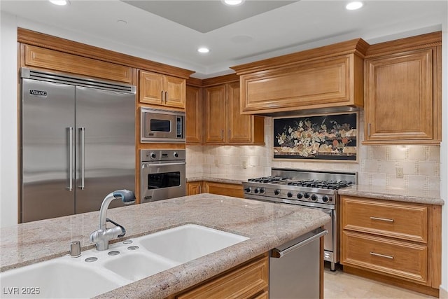 kitchen with a sink, decorative backsplash, built in appliances, and light stone counters