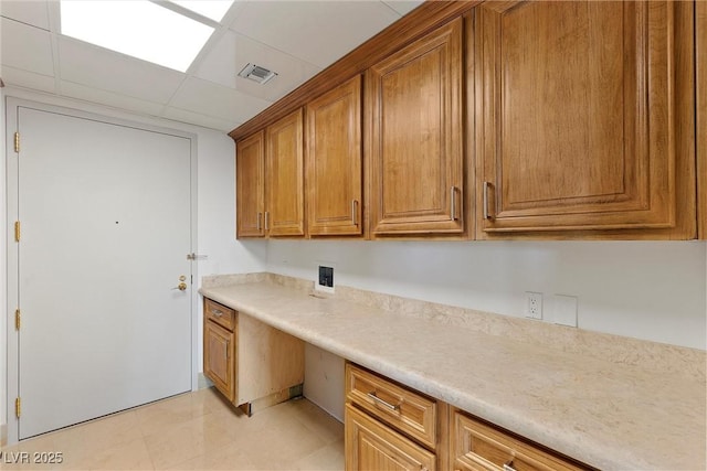 kitchen featuring visible vents, brown cabinets, built in desk, light countertops, and a paneled ceiling