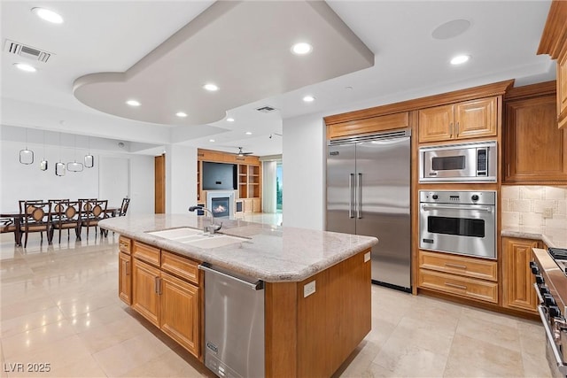 kitchen featuring light stone counters, visible vents, a kitchen island with sink, a sink, and built in appliances