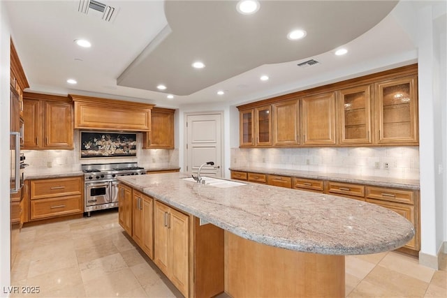 kitchen with double oven range, a center island with sink, visible vents, recessed lighting, and a sink