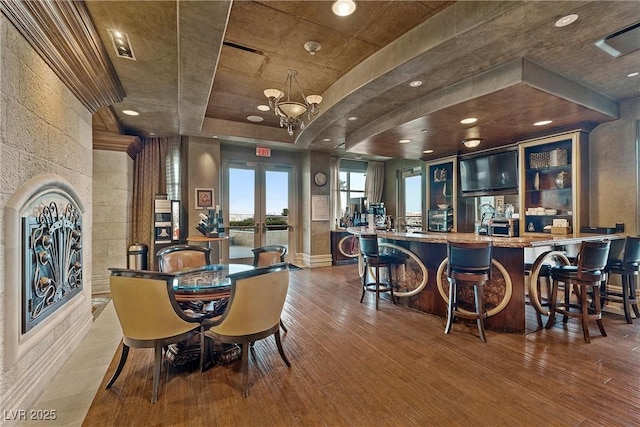 bar with a tray ceiling, french doors, wood finished floors, and a community bar