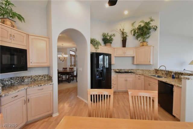 kitchen with light brown cabinets, arched walkways, a sink, black appliances, and light wood-type flooring