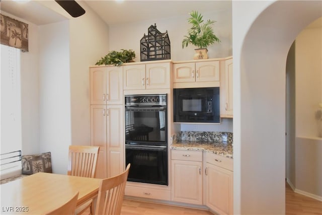 kitchen featuring light stone counters, light wood-type flooring, arched walkways, and black appliances