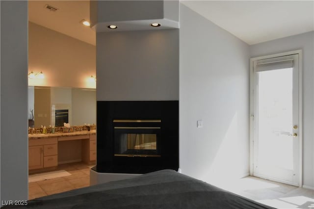 bedroom with light tile patterned floors, visible vents, connected bathroom, and a glass covered fireplace