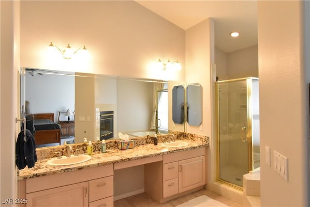 ensuite bathroom with double vanity, a shower stall, a fireplace, and a sink