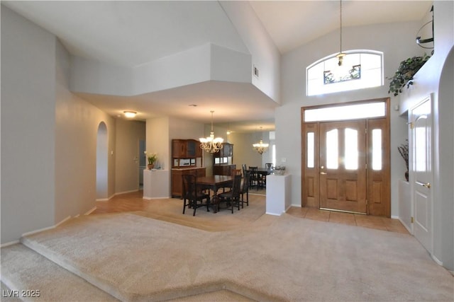 entryway featuring a notable chandelier, high vaulted ceiling, arched walkways, baseboards, and light colored carpet