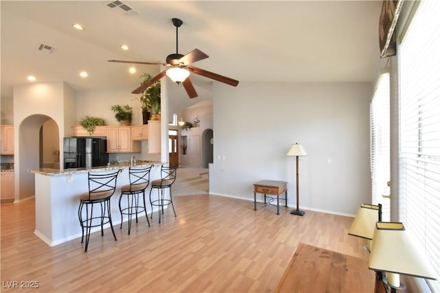 kitchen featuring visible vents, light brown cabinets, black fridge, a kitchen breakfast bar, and arched walkways