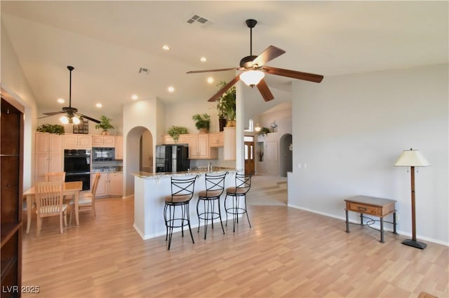 kitchen featuring visible vents, arched walkways, black appliances, and a breakfast bar