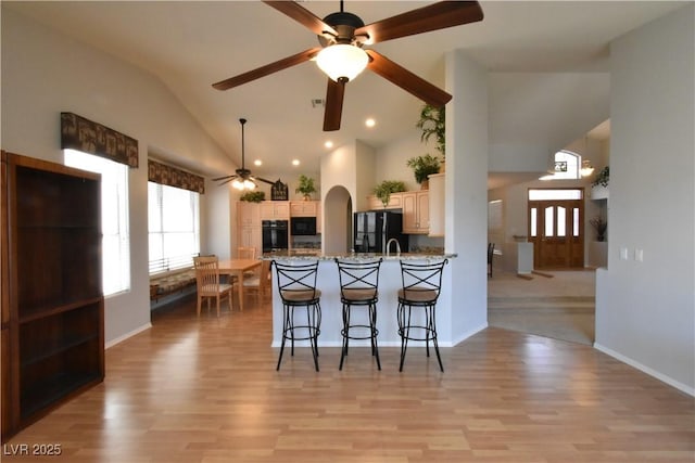 kitchen featuring a breakfast bar area, a peninsula, black appliances, and light wood-style flooring