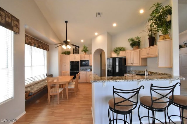 kitchen with visible vents, black appliances, light stone counters, arched walkways, and a peninsula