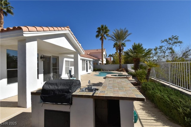 view of patio / terrace featuring a pool with connected hot tub, exterior kitchen, a fenced backyard, a grill, and a sink