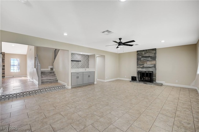 unfurnished living room with baseboards, visible vents, ceiling fan, stairs, and a large fireplace