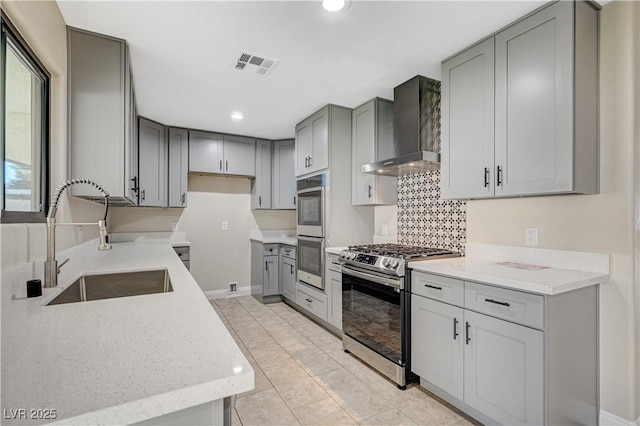 kitchen with visible vents, gray cabinetry, a sink, stainless steel appliances, and wall chimney exhaust hood