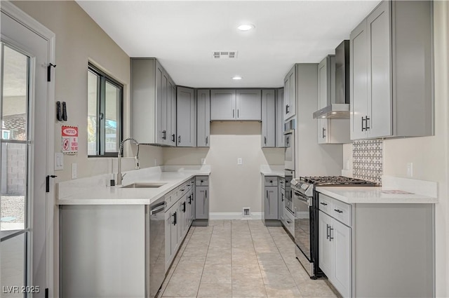 kitchen featuring gray cabinets, appliances with stainless steel finishes, wall chimney range hood, and a sink