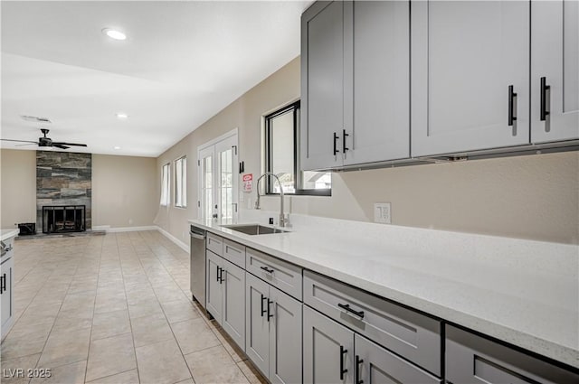 kitchen featuring a ceiling fan, gray cabinets, a tile fireplace, a sink, and dishwasher