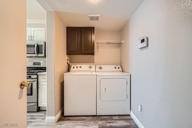 laundry room featuring visible vents, cabinet space, independent washer and dryer, and wood finished floors