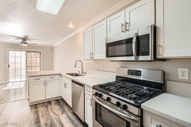 kitchen featuring crown molding, light wood-type flooring, appliances with stainless steel finishes, a peninsula, and a sink