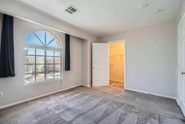 unfurnished bedroom featuring visible vents, baseboards, a walk in closet, and carpet flooring