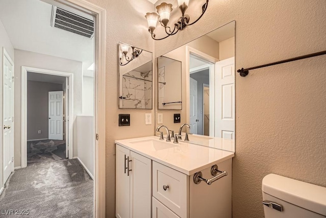 half bath with visible vents, toilet, vanity, and a textured wall