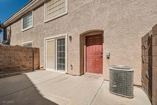 entrance to property featuring a patio, fence, central AC, and stucco siding