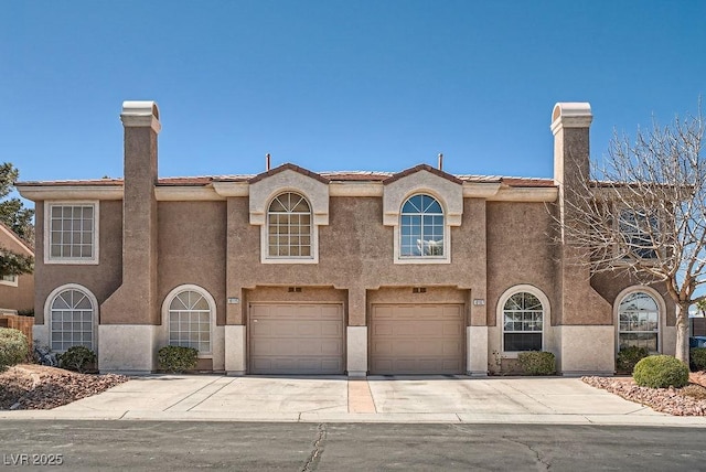 view of front of home with stucco siding, a garage, driveway, and a chimney