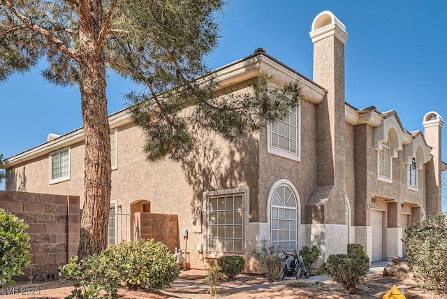 view of front of property with stucco siding, a chimney, and a garage