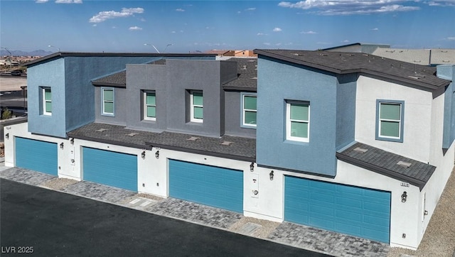 view of front facade featuring stucco siding, a residential view, a garage, and roof with shingles