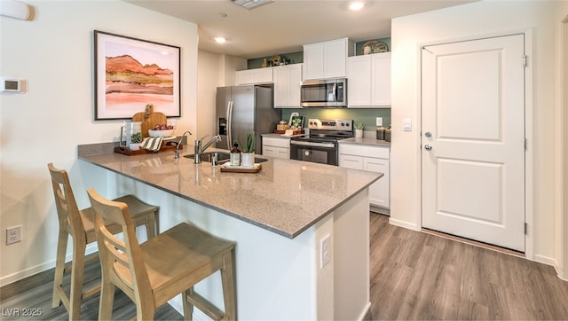 kitchen with a kitchen breakfast bar, stainless steel appliances, wood finished floors, white cabinetry, and a sink