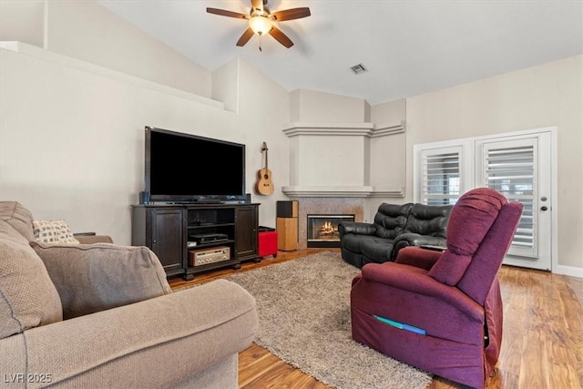 living room featuring vaulted ceiling, visible vents, a warm lit fireplace, and wood finished floors