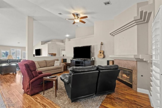 living room featuring visible vents, wood finished floors, a glass covered fireplace, high vaulted ceiling, and a ceiling fan