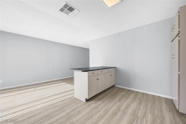 interior space with dark countertops, visible vents, baseboards, a peninsula, and light wood-style floors