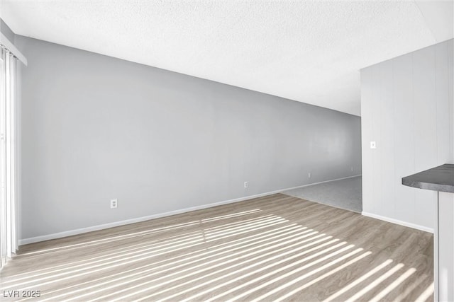 unfurnished living room featuring wood finished floors, baseboards, and a textured ceiling