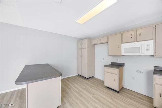 kitchen featuring white microwave, light wood finished floors, dark countertops, a peninsula, and cream cabinets