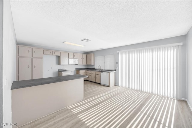 kitchen with dark countertops, white appliances, light wood-type flooring, and a sink