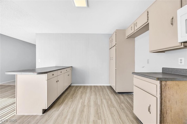 kitchen featuring dark countertops, a peninsula, and light wood-style flooring