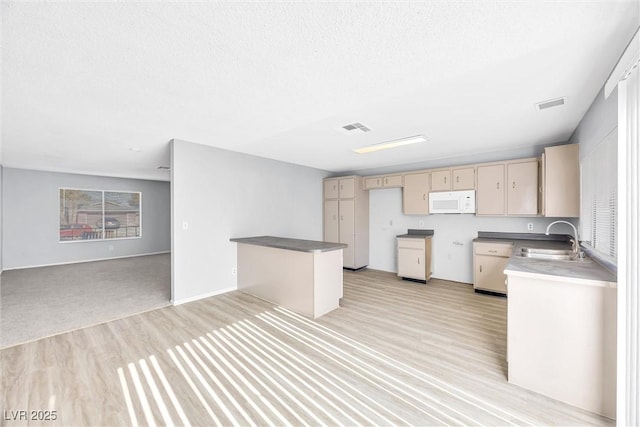 kitchen featuring open floor plan, white microwave, visible vents, and a sink