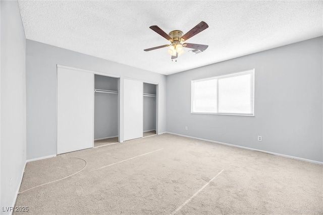 unfurnished bedroom with carpet flooring, a ceiling fan, two closets, and a textured ceiling